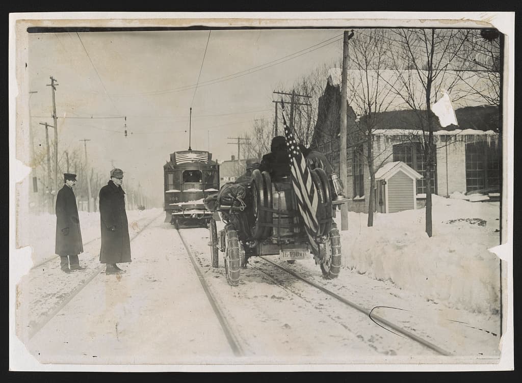 The Thomas Flyer behind a streetcar, flag flying, on winter roads.