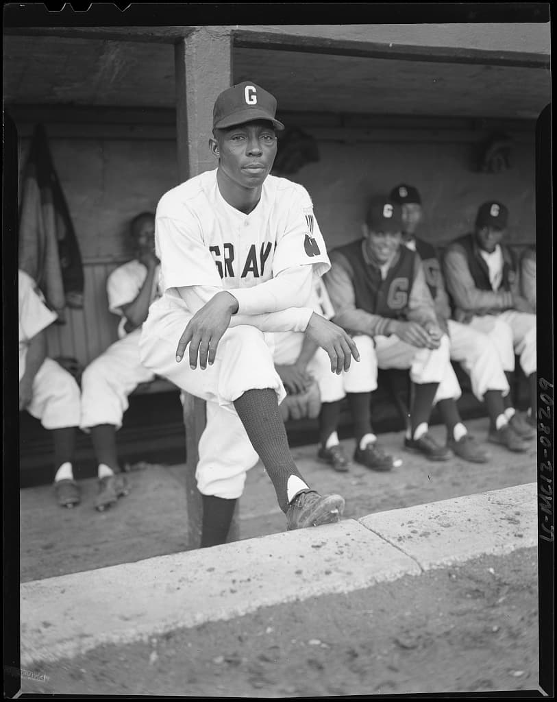 Manager Vic Harris standing in the dugout with his team behind him.